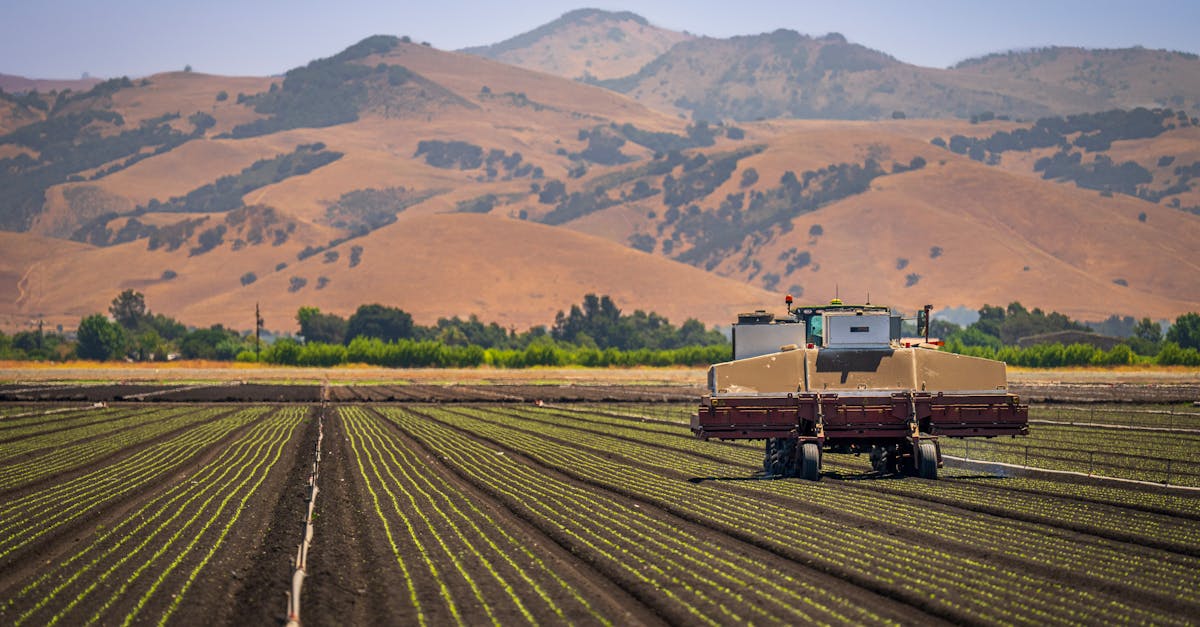 a farming machine operates on a sprawling agricultural field with hilly countryside views
