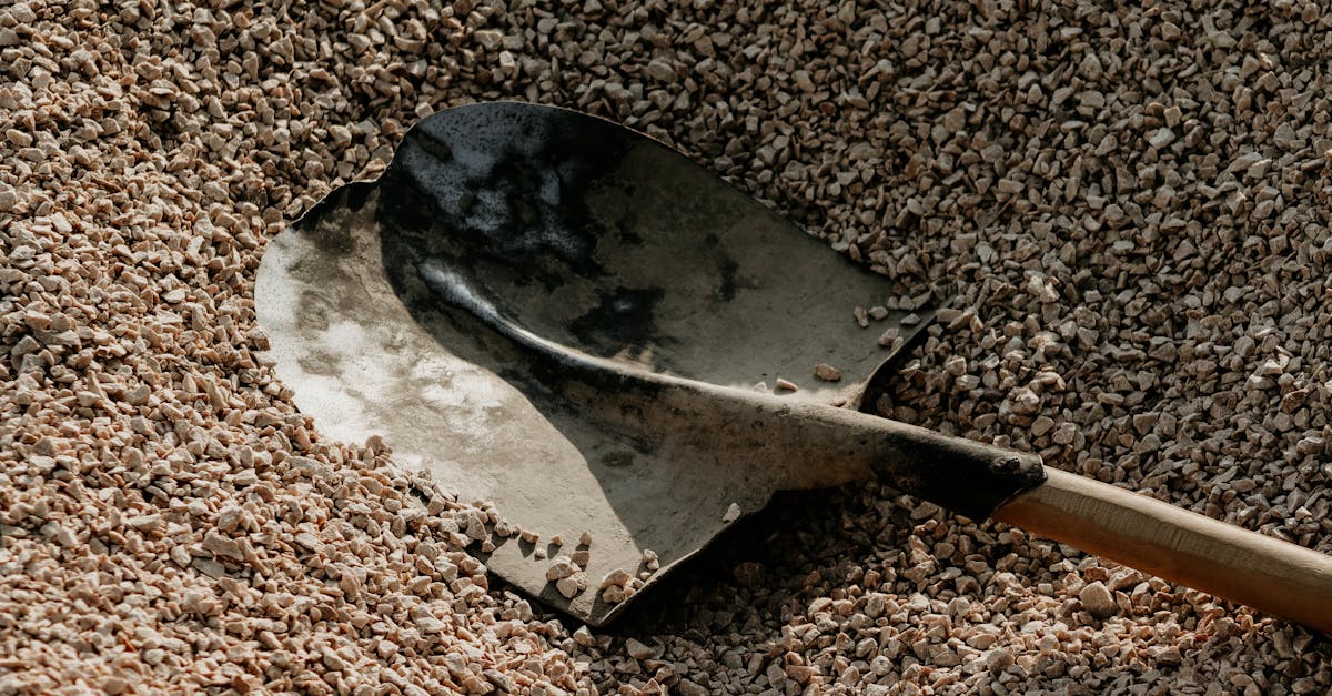 a metal shovel lying on a pile of small pebbles suggesting outdoor landscaping or construction acti