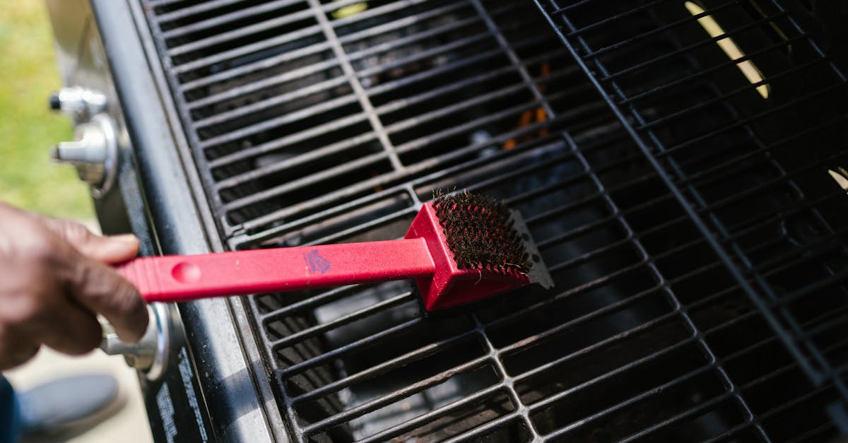 a person cleaning a barbecue grill with a red brush in daylight ideal for bbq enthusiasts