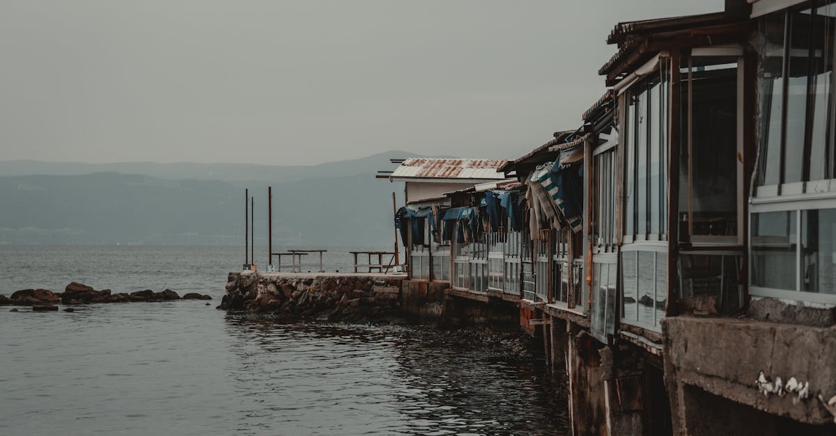 a series of rustic sheds perched on a weathered pier over a tranquil lake under an overcast sky