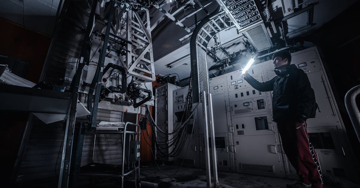 a technician using a flashlight to examine equipment in a dimly lit industrial control room
