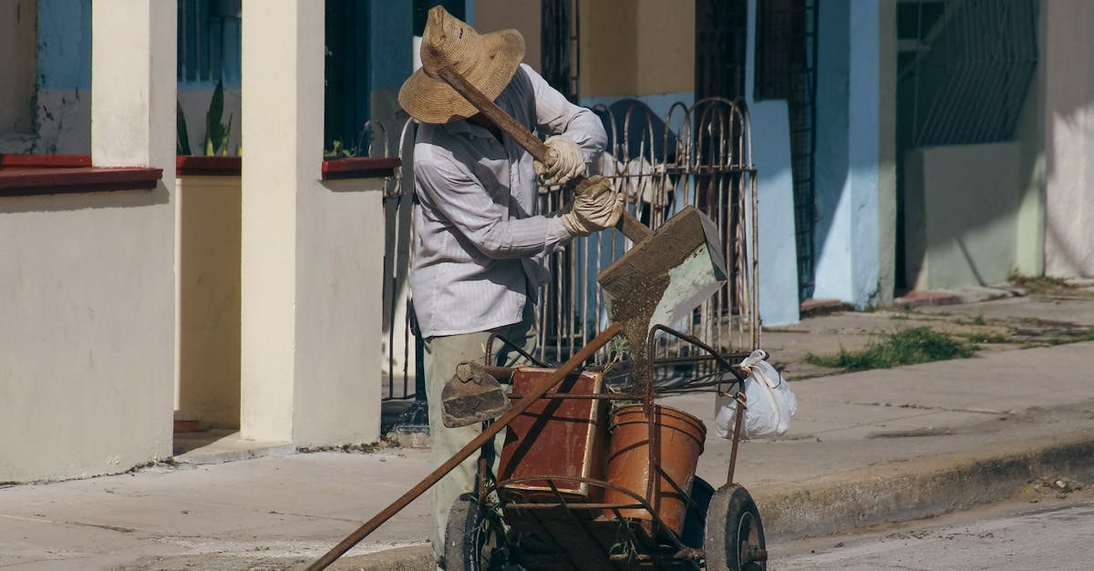 a worker in a hat sweeps and cleans a city sidewalk with a cart and broom during the day