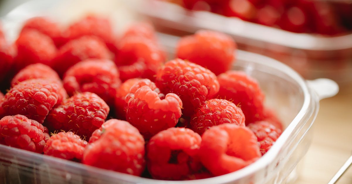 appetizing red ripe raspberries in small plastic container placed on wooden surface in daylight
