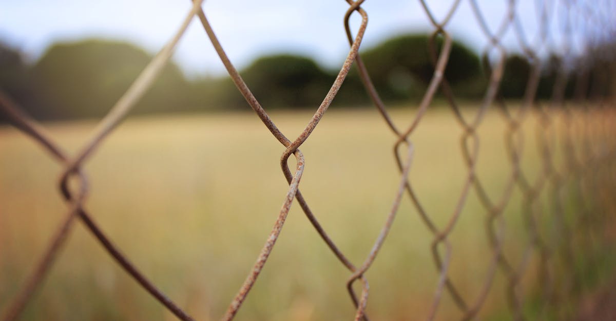 close up of a rusty chain link fence with a serene meadow in the background