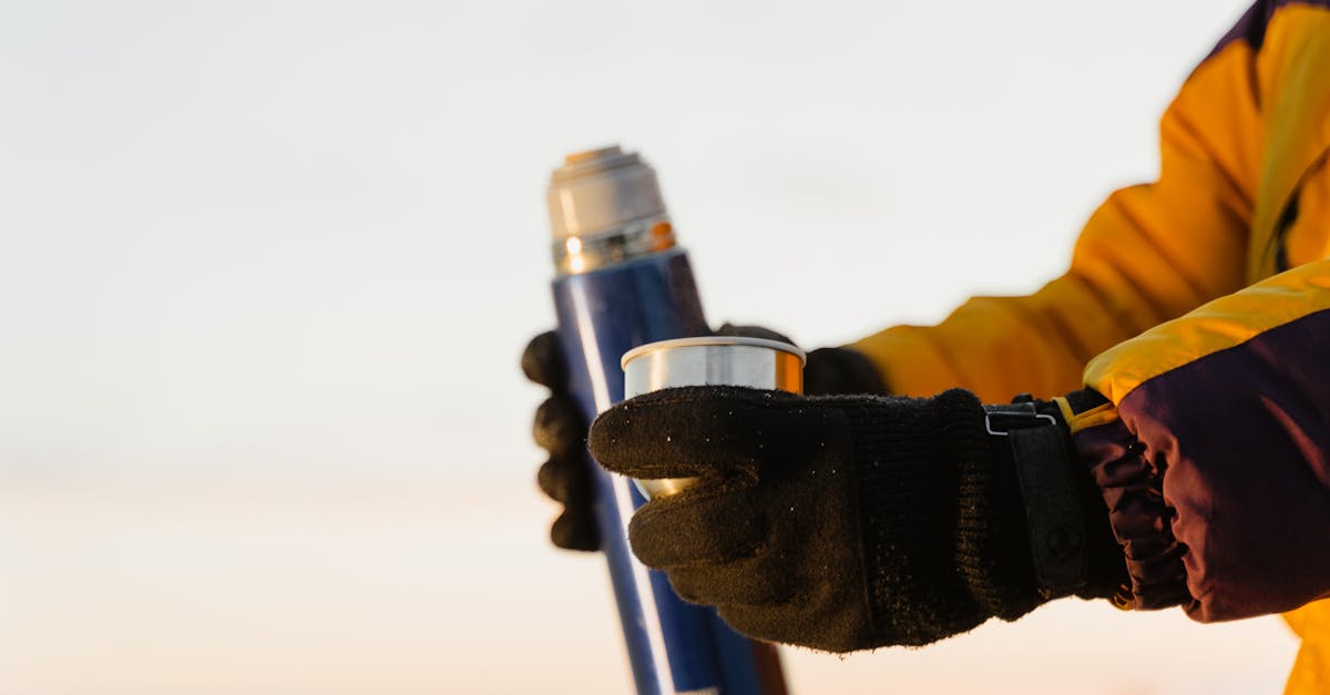 close up of gloved hands holding a thermos and cup outdoors in winter