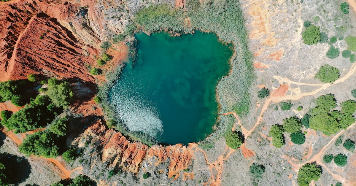 drone view of turquoise water of small pond surrounded by rough stony formation with green plants