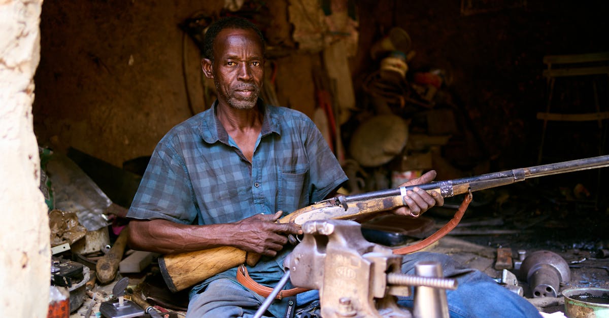 focused portrait of an artisan in a workshop holding a handcrafted rifle surrounded by tools