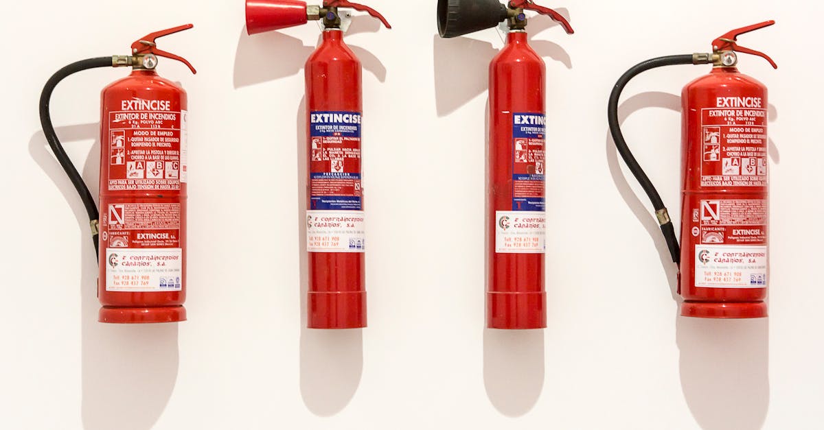 four red fire extinguishers hanging on a clean white wall in an orderly fashion