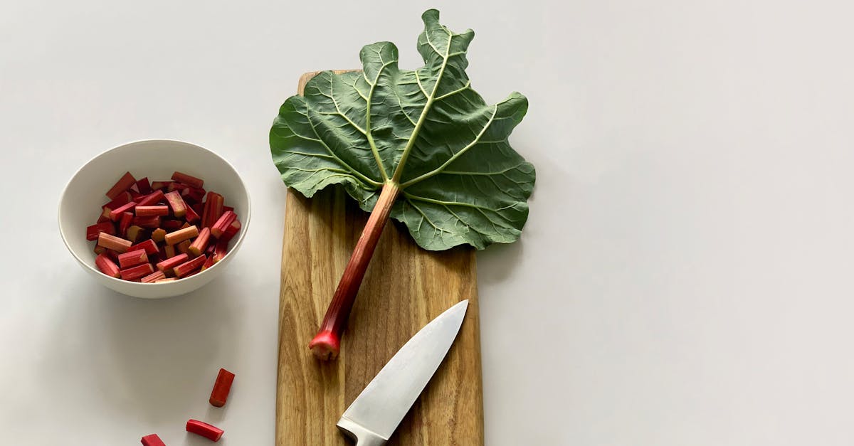 fresh rhubarb stalk and leaves on a wooden cutting board with a knife ready for cooking