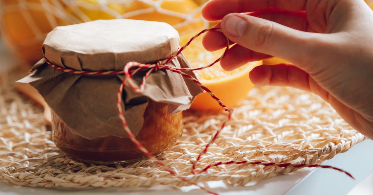 homemade jam jar with hand tying string surrounded by fresh oranges in warm lighting