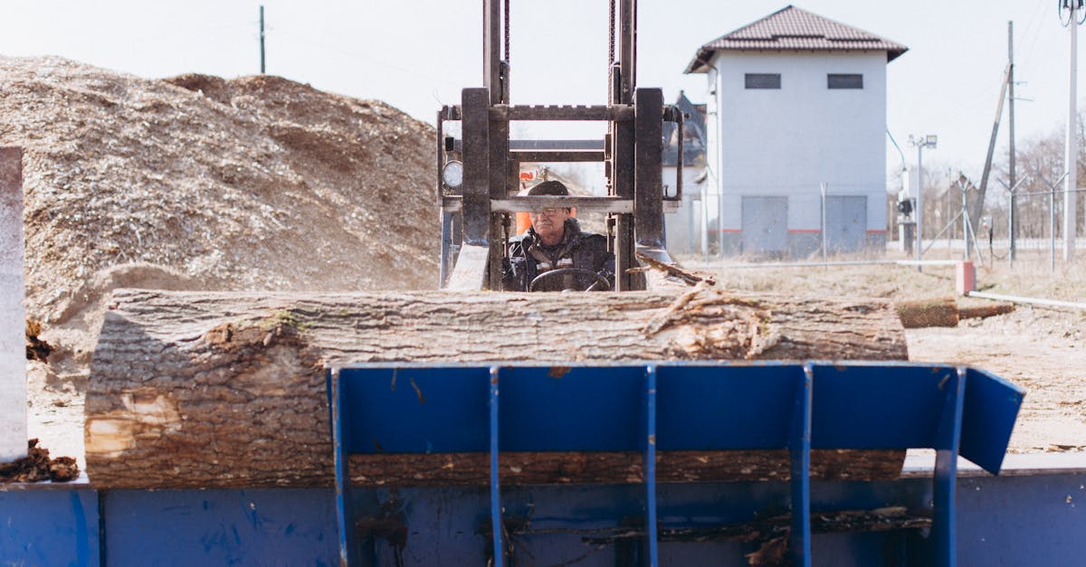 man driving a forklift carrying logs at an outdoor industrial site
