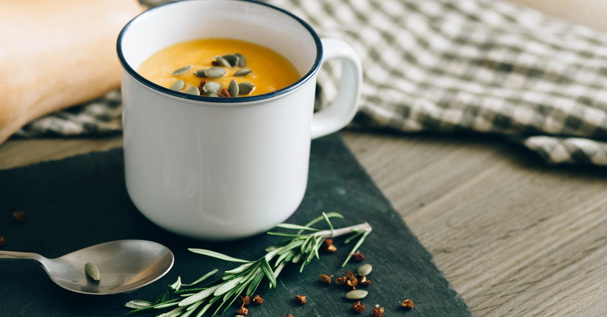 warm pumpkin soup garnished with seeds and herbs in an enamel mug perfect for fall comfort food